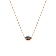 A delicate rose gold chain necklace featuring a small, polished gold crescent-shaped setting holding a round, dark gray diamond, presented on a solid white background.