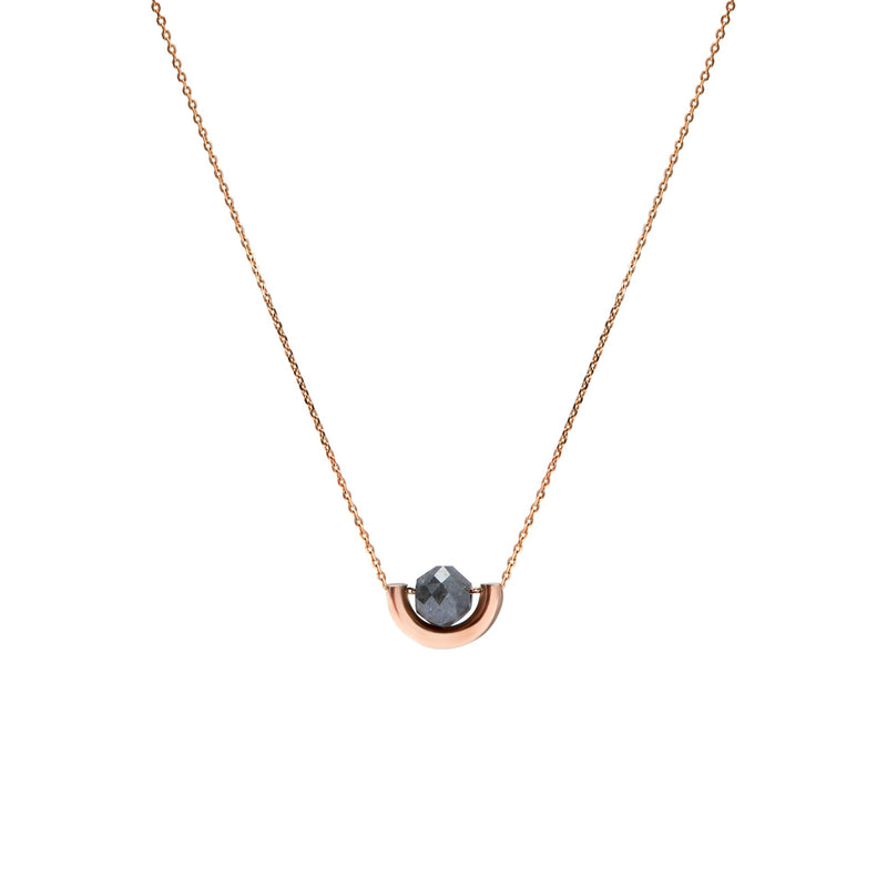 A delicate rose gold chain necklace featuring a small, polished gold crescent-shaped setting holding a round, dark gray diamond, presented on a solid white background.