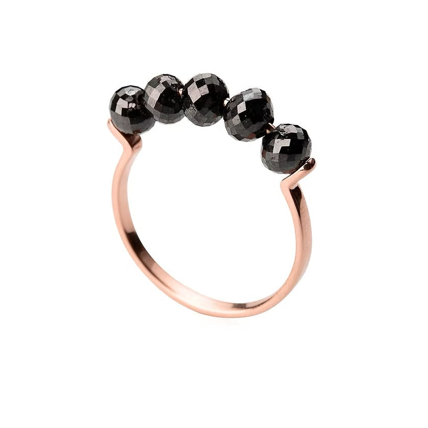 A rose gold ring featuring five faceted black diamonds beads set across the top, photographed on a clean white background.