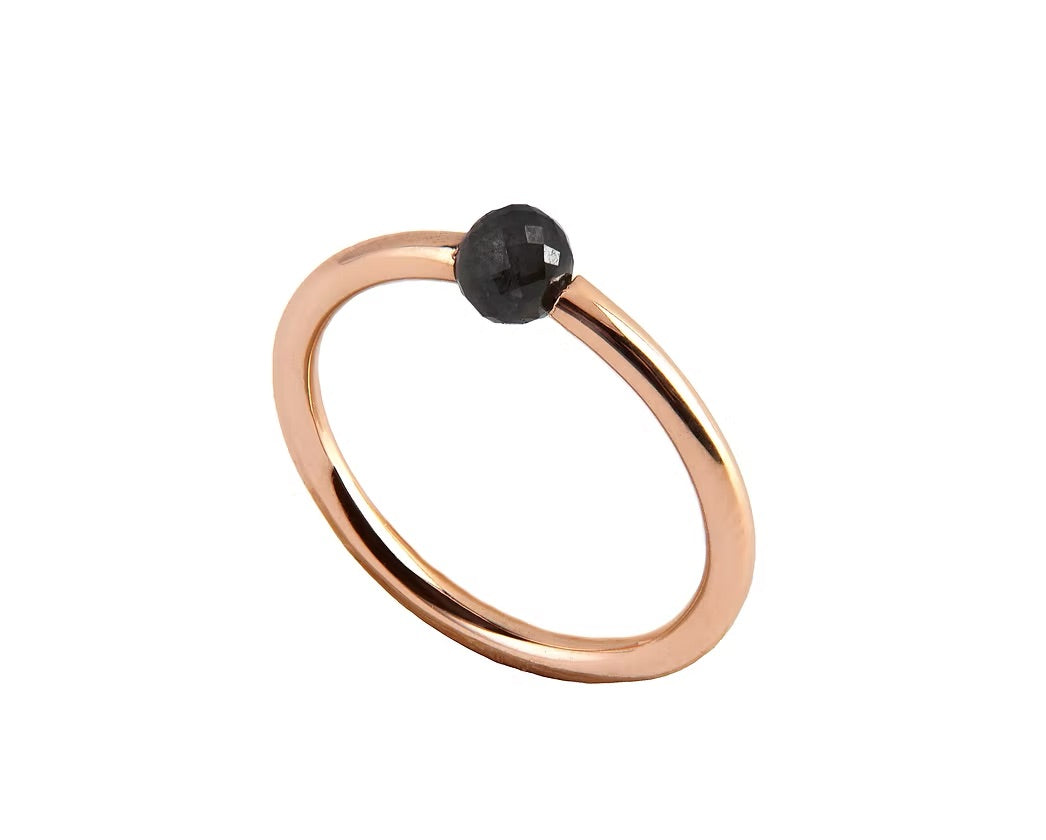 A minimalist rose gold ring featuring a single, small, round black faceted diamond, shown on a plain white background.