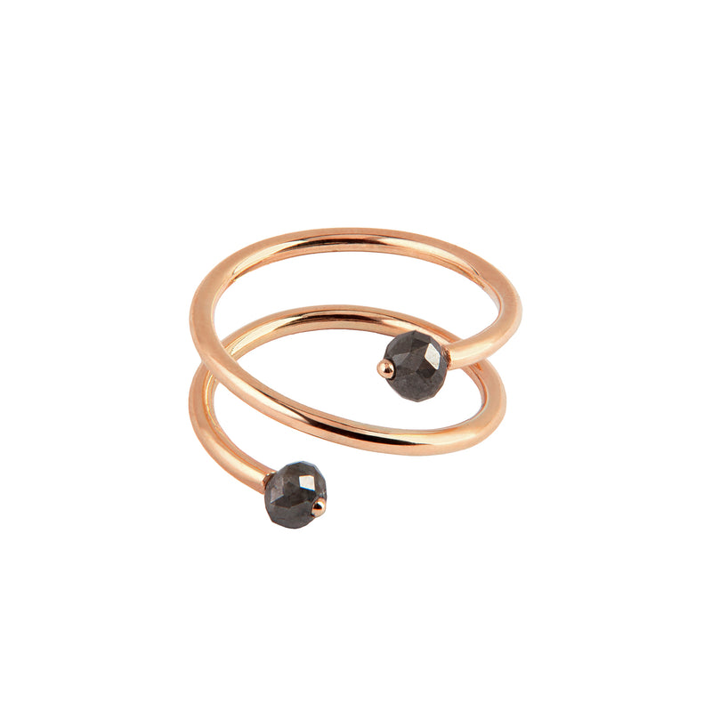 A twisted open wrap ring in polished rose gold, featuring two small faceted dark gray gemstones at the ends, shown on a plain white background.