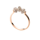 A rose gold ring featuring three small, raw-cut diamond stones set across the top, shown against a plain white background.
