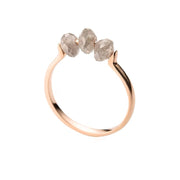 A rose gold ring featuring three small, raw-cut diamond stones set across the top, shown against a plain white background.