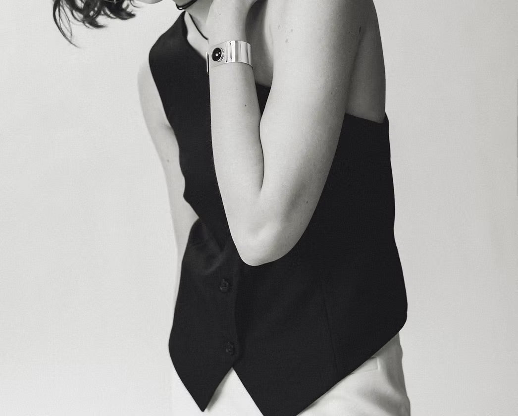 A black sleeveless vest with a unique asymmetrical button closure, worn by a model in a black and white photograph.