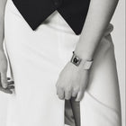 A close-up black and white photo of a person wearing a distinctive silver cuff bracelet with a black amber on their wrist, paired with a white skirt and dark top.