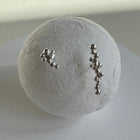 Two silver stud earrings with small clustered bead-like details, displayed on a round white textured stand against a light gray background.