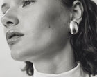 A close-up black and white photograph of a woman wearing a large, oval, polished silver earring.