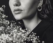 A close-up black and white photograph of a woman wearing a distinctive circular earring with a dark amber and light outer ring, styled with baby's breath flowers.