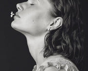 A black and white close-up portrait of a woman, wearing a silver earrings, set against a dark background.