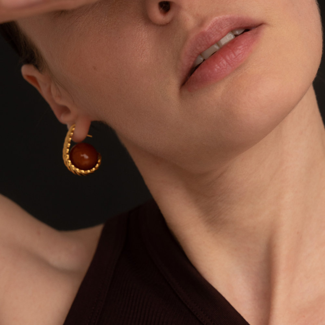 Close-up of a model wearing a gold crescent-shaped hoop earring with a round amber stone.