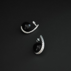 A pair of silver crescent-shaped earrings with smooth black oval stones, photographed on a dark gray background.