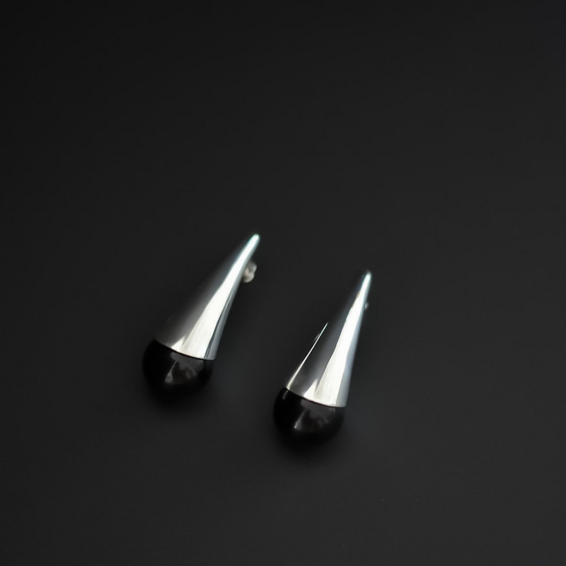 A pair of modern geometric stud earrings with polished silver spike tops and smooth black spherical bases, displayed on a dark black background.