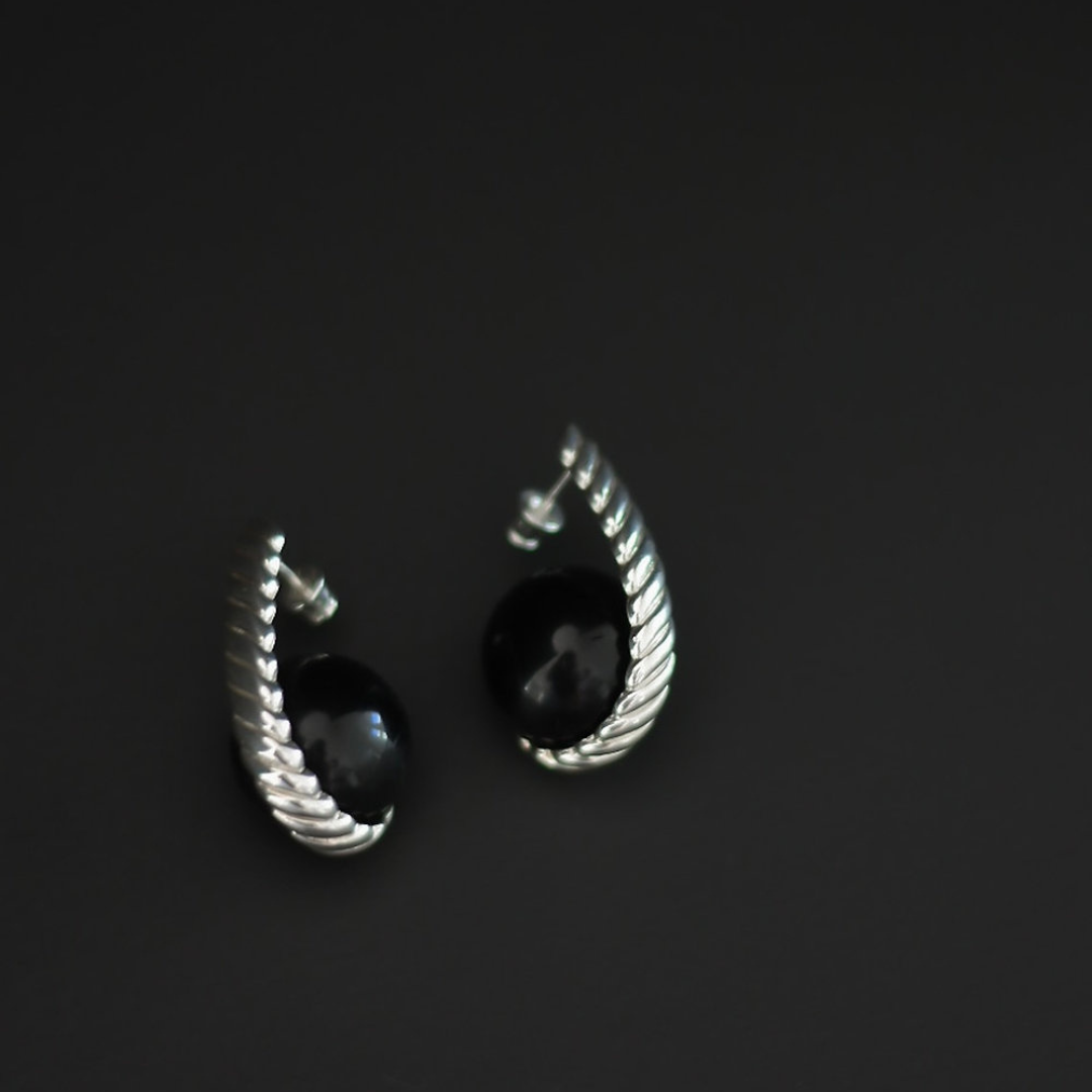 A pair of silver-toned twisted hoop earrings with round black gemstone centers, photographed on a dark gray background.
