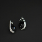 A pair of silver-toned twisted hoop earrings with round black gemstone centers, photographed on a dark gray background.
