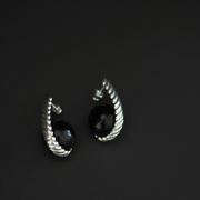 A pair of silver-toned twisted hoop earrings with round black gemstone centers, photographed on a dark gray background.