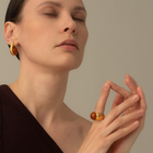 A close-up lifestyle shot of a woman with her eyes closed, wearing a gold ring with a round amber cabochon on her finger and a matching gold hoop earring.