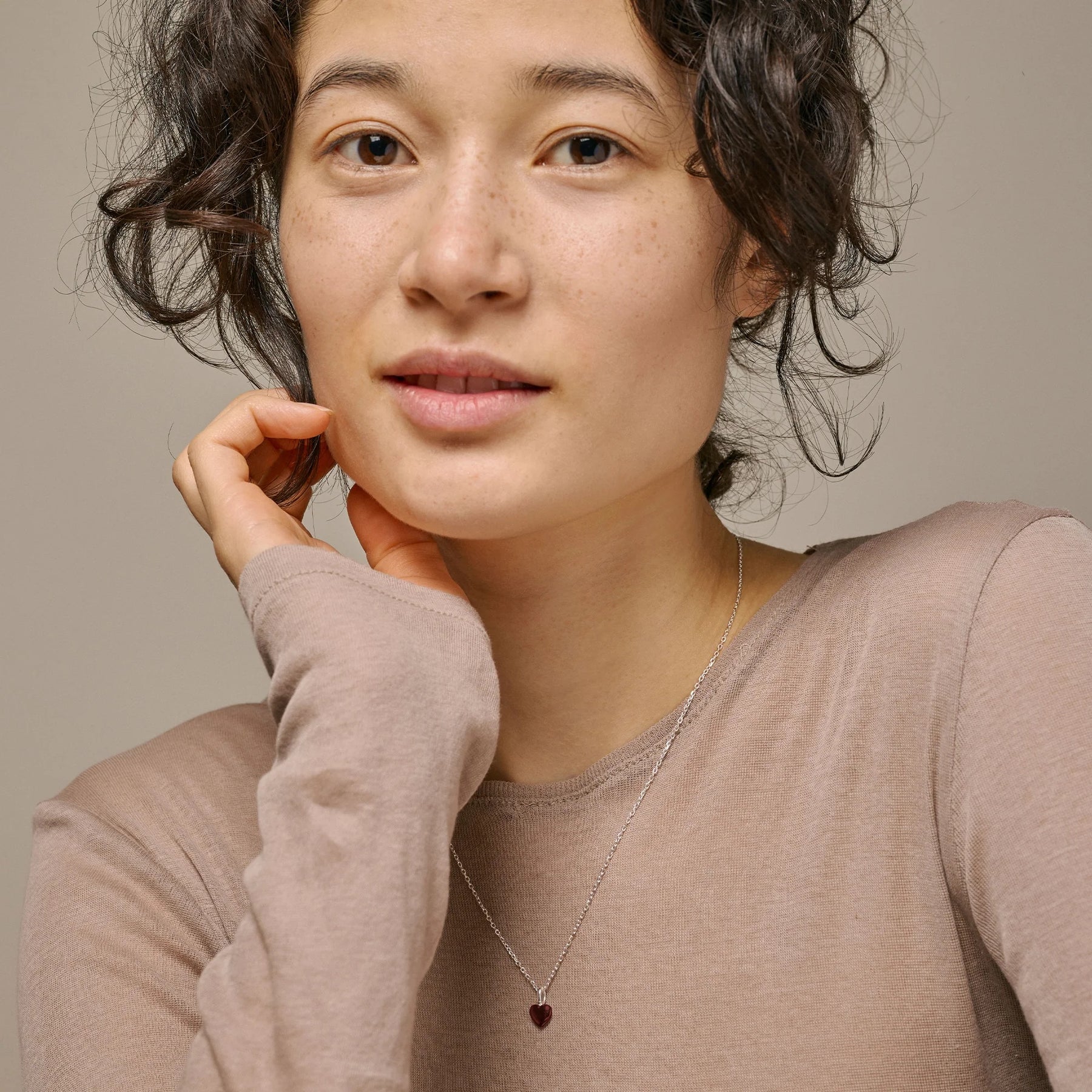 Woman wearing a beige sweater and heart-shaped necklace.