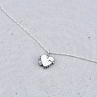 A delicate silver necklace with a small heart-shaped pendant resting on a textured light gray surface.