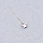 A delicate silver chain necklace with a small, polished silver heart pendant, resting on a textured light gray surface.