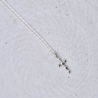 A delicate silver cross pendant necklace on a fine silver chain, displayed on a textured light gray concrete surface.