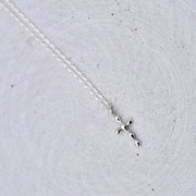 A delicate silver cross pendant necklace on a fine silver chain, displayed on a textured light gray concrete surface.
