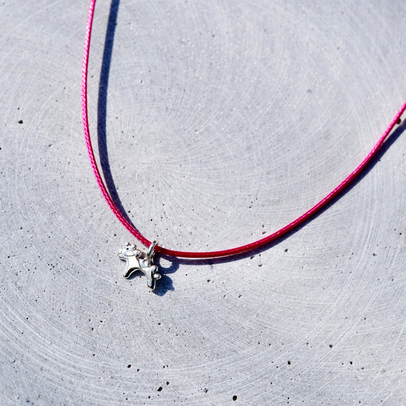 A vibrant pink cord necklace with a small silver-toned star charm, laid flat on a textured light gray concrete surface.