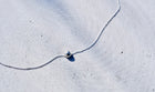 A delicate silver chain necklace with a small silver bead pendant, laid out on a textured light gray concrete surface.