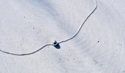 A delicate silver chain necklace with a small silver bead pendant, laid out on a textured light gray concrete surface.
