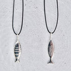 Two silver fish-shaped pendant necklaces on black cords, displayed against a textured light gray background.