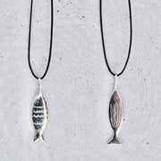 Two silver fish-shaped pendant necklaces on black cords, displayed against a textured light gray background.