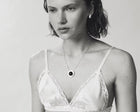 A close-up black and white lifestyle shot of a woman wearing a delicate silver chain necklace with a circular pendant featuring a dark amber at the center.