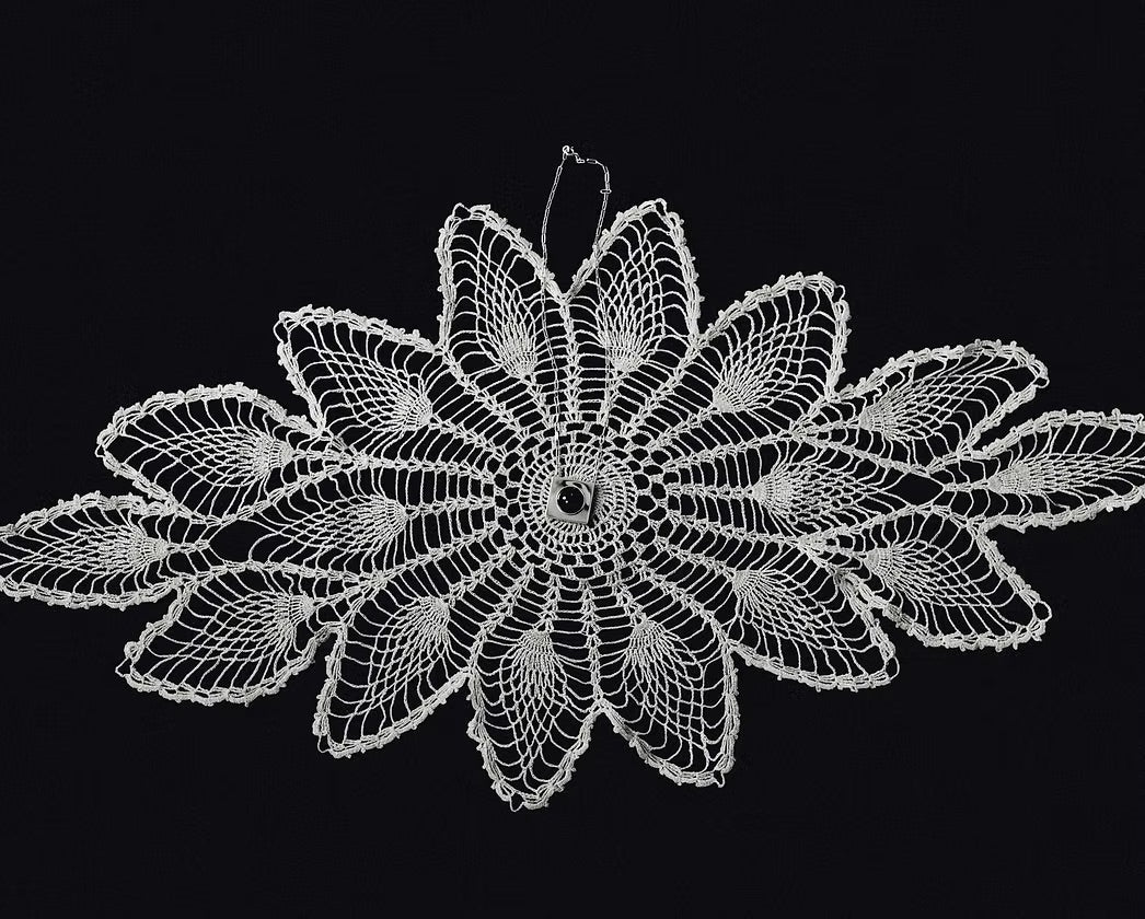 A white crocheted lace doily with a detailed floral pattern, displayed flat against a solid black background.