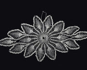 A white crocheted lace doily with a detailed floral pattern, displayed flat against a solid black background.