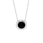 A minimalist silver pendant necklace featuring a circular silver frame with a smooth, black amber center, suspended from a delicate silver chain against a solid white background.
