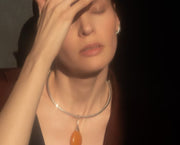 A close-up lifestyle shot of a woman wearing a silver-toned double-ring collar necklace with a teardrop-shaped amber pendant, set against a dark background.