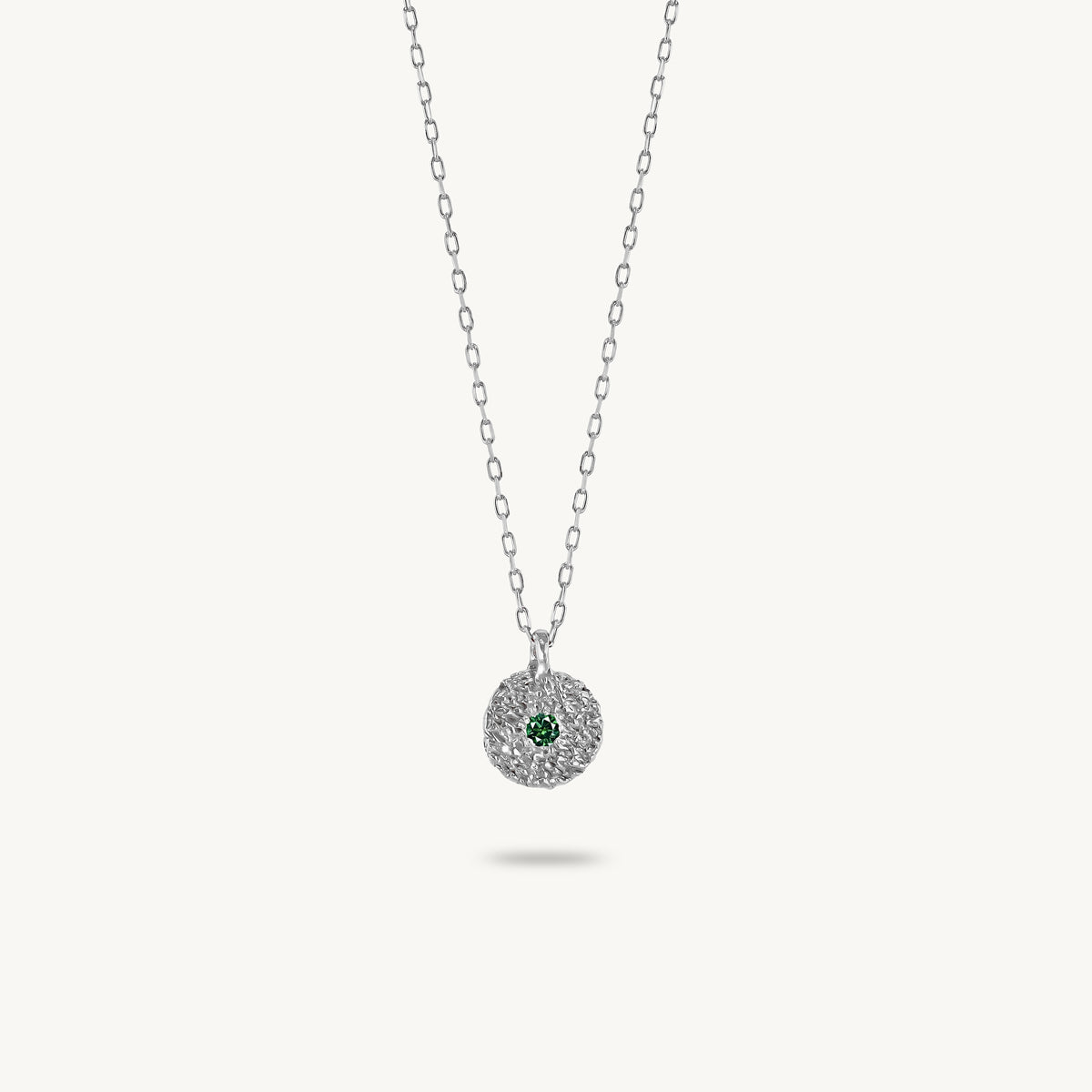 Sterling silver chain necklace featuring a round, textured disc pendant with a small emerald set in the center.
