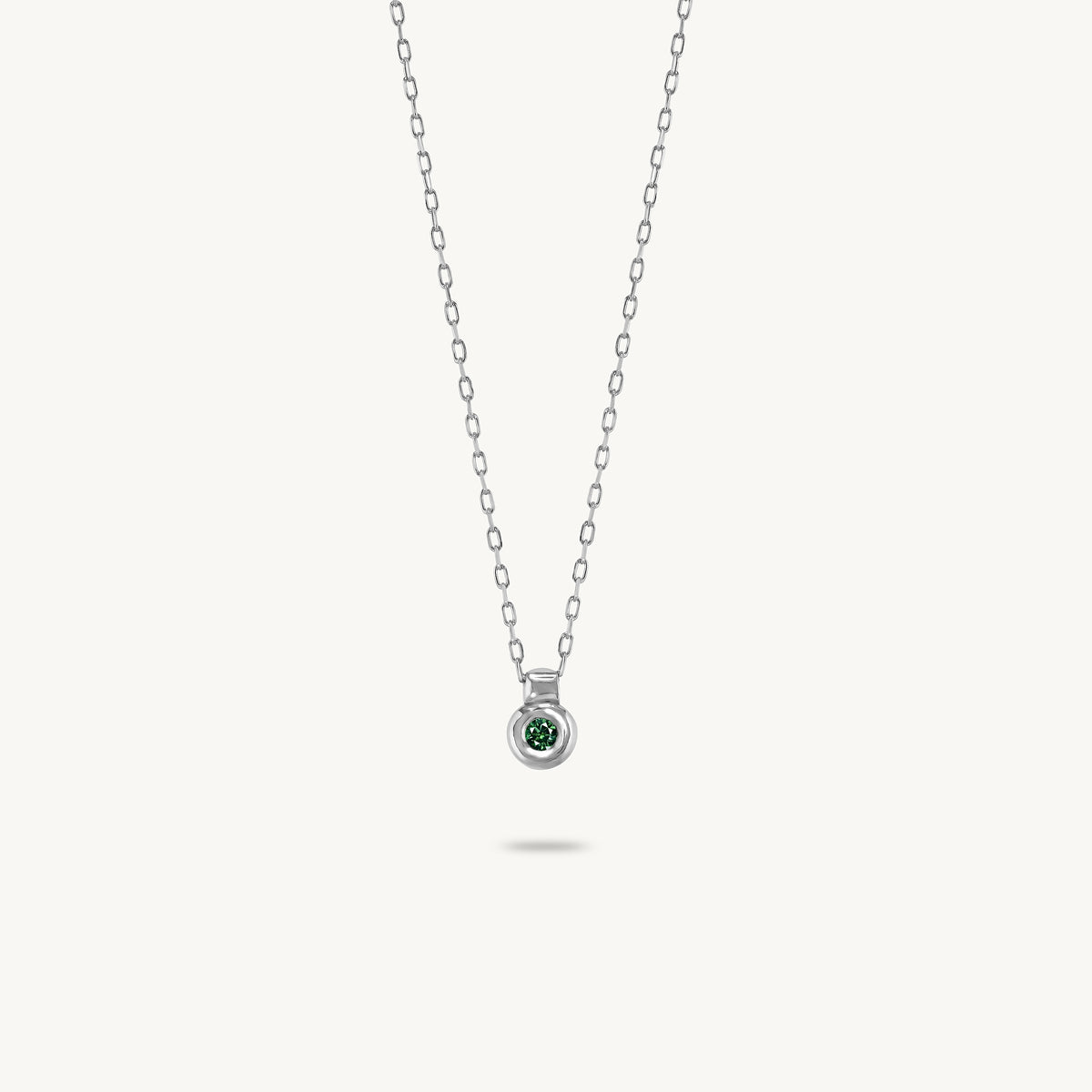 A silver pendant featuring a smooth, sculptural bezel framing a single central emerald.