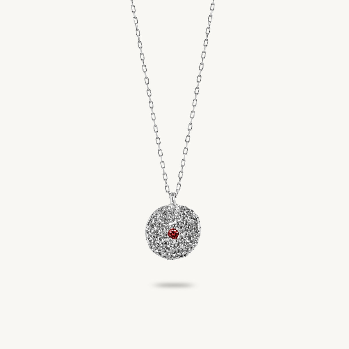 Sterling silver chain necklace featuring a round, textured disc pendant with a small red sapphire set in the center