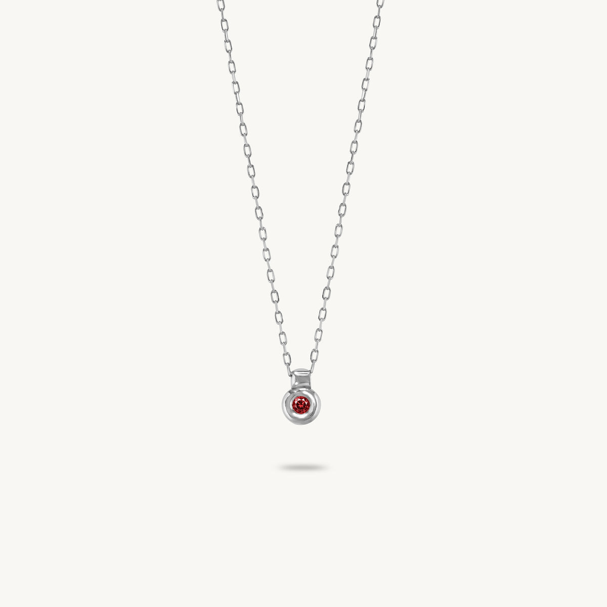 A silver pendant featuring a smooth, sculptural bezel framing a single central red sapphire.