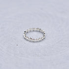 A silver textured band ring resting on a light gray, subtly textured circular surface.