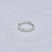 A silver textured band ring resting on a light gray, subtly textured circular surface.