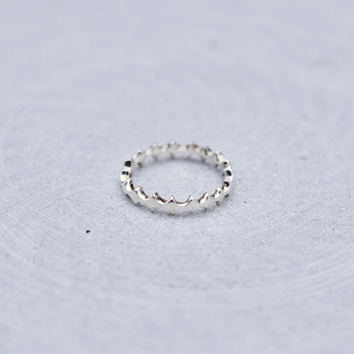 A silver textured band ring resting on a light gray, subtly textured circular surface.