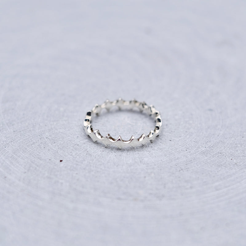 A silver textured band ring resting on a light gray, subtly textured circular surface.