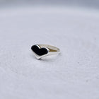 A silver heart-shaped ring, resting on a textured light gray surface.