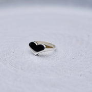 A silver heart-shaped ring, resting on a textured light gray surface.