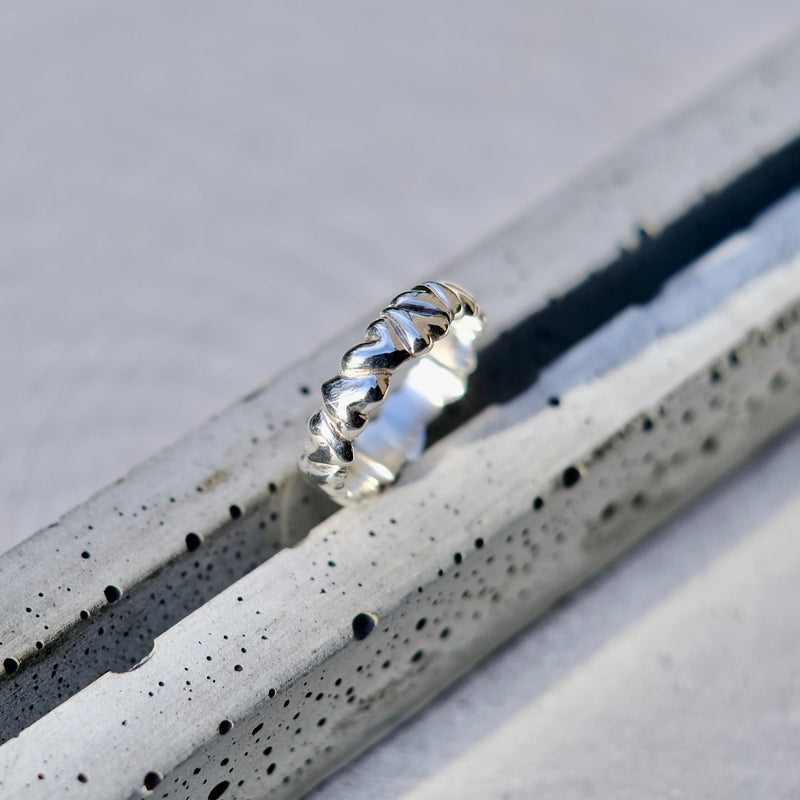A silver ring with a textured, ridged band, resting on a speckled gray concrete surface.