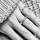 A close-up of a hand wearing two silver rings, one textured band and one thinner twisted band, resting on a gray knitted blanket.