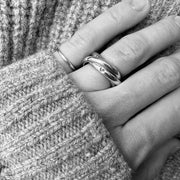 A close-up black and white photo of a person's hand resting against a chunky knit sweater, wearing two silver rings.