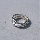 Three interlocked silver rings on a textured light gray surface.
