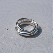 Three interlocked silver rings on a textured light gray surface.